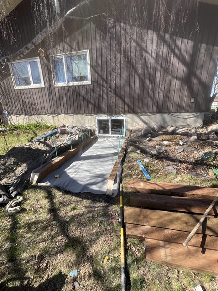 Egress window installation job site — excavation and concrete pad work in progress, Calgary