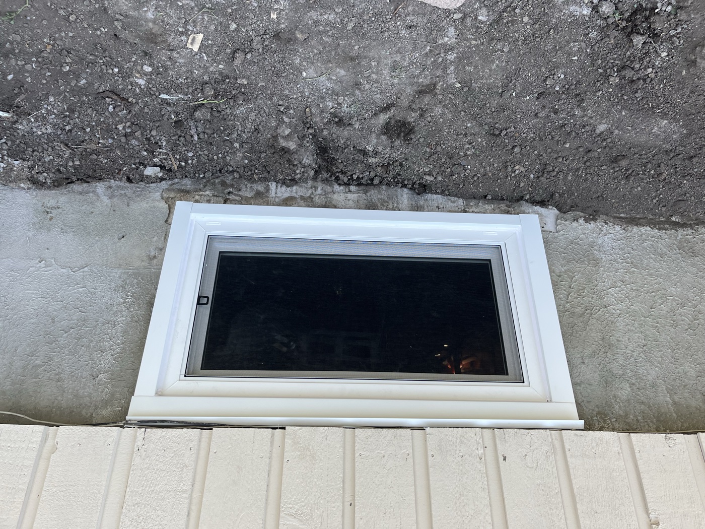 Egress hopper window exterior view with galvanized well — Calgary home