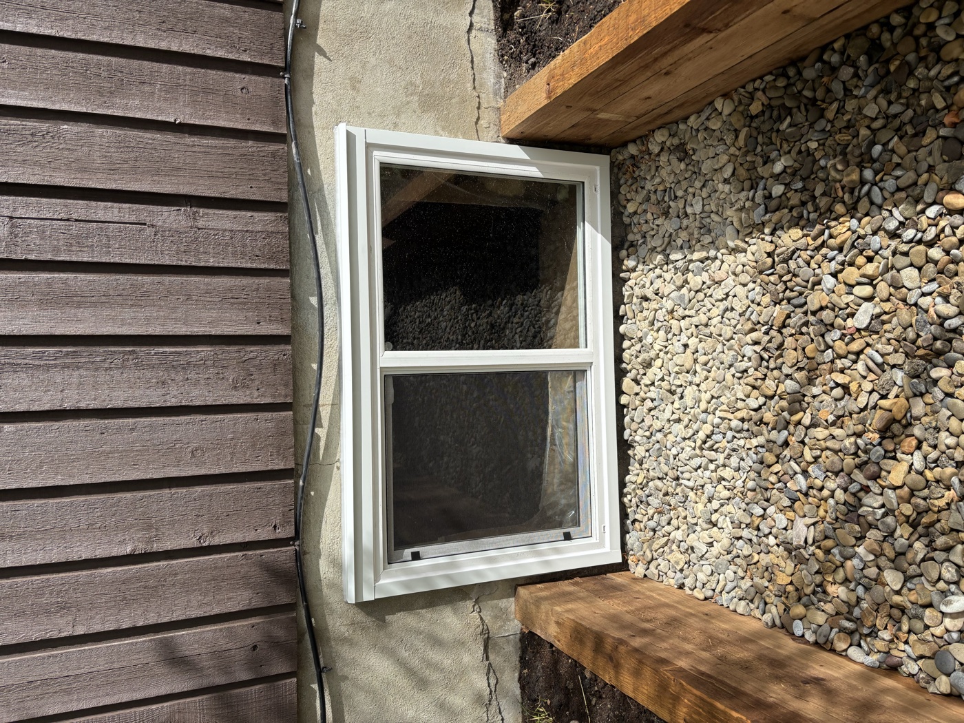 Exterior egress window installation complete with well and stone — Calgary